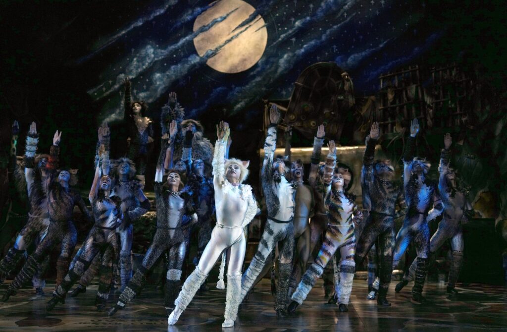 The full company of Cats the Musical posed beneath a giant moon