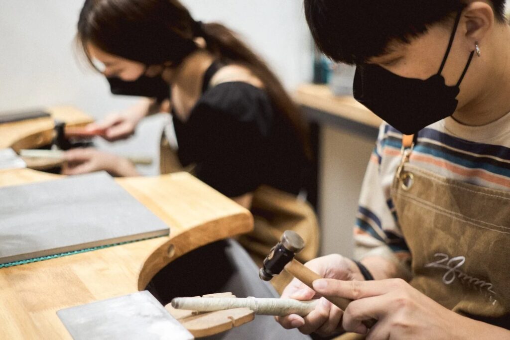 A couple hammering silver rings at a workbench during the 28MM Studios Make-A-Ring workshop